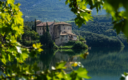 Historisches Gebäude am See, umgeben von grüner Landschaft und Bäumen.