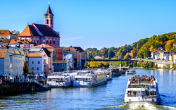 Bunte Gebäude und Boote an einem Fluss, Kirche im Hintergrund.
