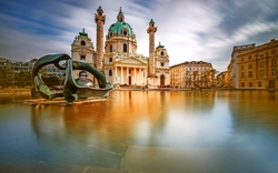 Barockkirche bei Tag, reflektiert im Wasser eines Springbrunnens im Vordergrund.