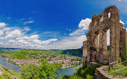 Panoramablick auf Ruinen mit Fluss und Hügeln im Hintergrund bei sonnigem Wetter.
