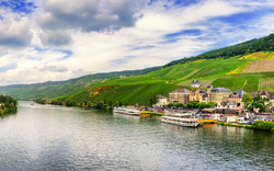 Flusslandschaft mit Weinbergen, Häusern und Booten unter blauem Himmel.