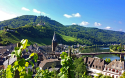 Stadtansicht mit Kirche und Hügeln im Hintergrund, Fluss im Vordergrund.