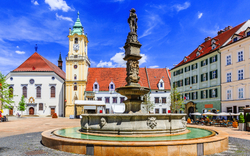 Historischer Platz mit Brunnen und Gebäuden unter klarem Himmel.