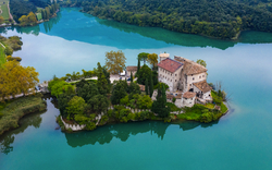Luftaufnahme einer Burg auf einer kleinen Insel in einem See mit umgebender Waldlandschaft.