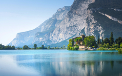 Burg am Ufer eines Sees, umgeben von Bergen und Bäumen.