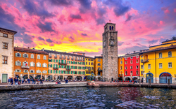 Platz mit farbigen Gebäuden und hohem Turm am Wasser bei Sonnenuntergang.