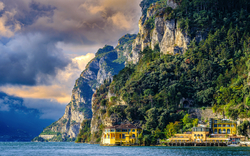 Küstenlandschaft mit bewaldeten Klippen und Häusern am Seeufer.