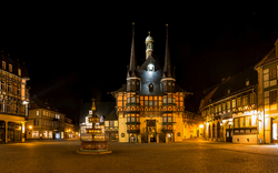 Historisches Rathaus mit Fachwerkhäusern bei Nacht beleuchtet.