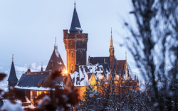 Mittelalterliches Schloss im Winter mit Schneebedeckung und abendlicher Beleuchtung.