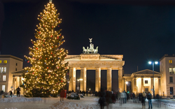 Brandenburger Tor mit beleuchtetem Weihnachtsbaum im Schnee bei Nacht.