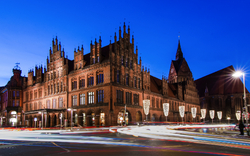 Historisches Gebäude bei Nacht mit beleuchteten Fassaden und verschwommenen Autolichtern.