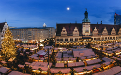 Weihnachtsmarkt bei Nacht mit geschmücktem Baum und Buden auf einem Platz in der Stadt.