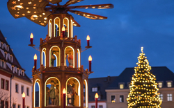 Holzpyramide und Weihnachtsbaum auf einem Weihnachtsmarkt bei Abenddämmerung