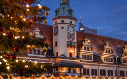 Weihnachtlich beleuchtetes historisches Gebäude bei Dämmerung, neben einem geschmückten Baum.