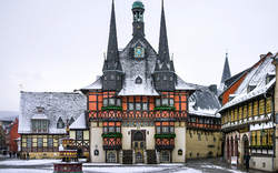 Verschneites Fachwerk-Rathaus mit Türmen und Marktbrunnen in einer Altstadt.