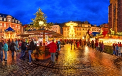 Weihnachtsmarkt am Abend mit erleuchteten Ständen und Menschen auf einem Kopfsteinpflaster.