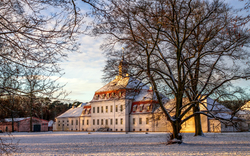 Historisches Gebäude im Winter mit verschneitem Garten und Bäumen.