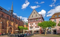 Historischer Platz mit Fachwerkhaus, Kirche und Straßencafé bei sonnigem Wetter.