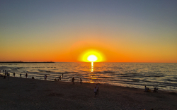 Sonnenuntergang am Strand mit Menschen im Vordergrund.