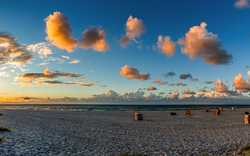Strandlandschaft bei Sonnenuntergang mit verstreuten Wolken und Strandkörben.