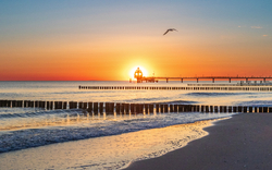 Sonnenuntergang am Strand mit Seebrücke und Möwe am Himmel.