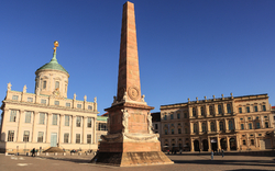 Historischer Platz mit Obelisk und klassizistischen Gebäuden bei klarem Himmel.