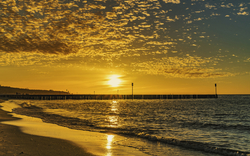 Sonnenuntergang am Strand von Kołobrzeg, Polen, mit Blick auf die Ostsee und die Seebrücke.
