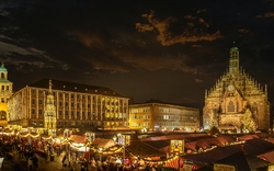 Nürnberger Christkindlesmarkt am Abend mit beleuchteten Ständen und Kirche im Hintergrund.