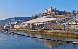 Festung auf Hügel über Fluss in winterlicher Stadtlandschaft.