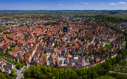 Luftaufnahme einer mittelalterlichen, kreisförmigen Stadt mit roten Dächern und grüner Umgebung.