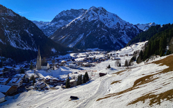 Bergdorf im Schnee mit Kirche und umliegenden Bergen bei klarem Himmel.