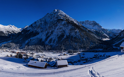 Winterliche Berglandschaft im Sonnenschein mit schneebedeckten Gipfeln und Tal.