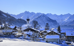 Verschneites alpenländisches Dorf mit Kirche und Bergen im Hintergrund.