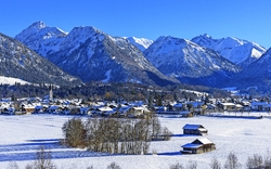Verschneites Dorf mit Bergen im Hintergrund und klarem, blauem Himmel.