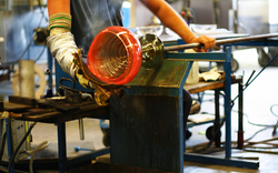 Person formt Glas mit Blasrohr in einer Werkstatt.