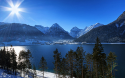 Winterliche Berglandschaft mit Schneebedeckten Bergen und einem klaren See im Vordergrund.