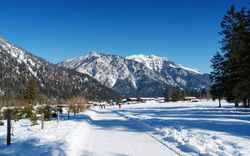 Winterliche Landschaft mit schneebedeckten Bergen und Bäumen unter blauem Himmel.