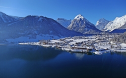 Winterliche Ansicht eines Sees mit schneebedeckten Bergen und Dorf im Hintergrund.