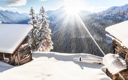Schneebedeckte Hütten in winterlicher Berglandschaft bei Sonnenschein