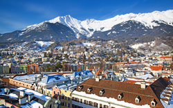 Winterliche Stadtansicht mit verschneiten Bergen im Hintergrund.