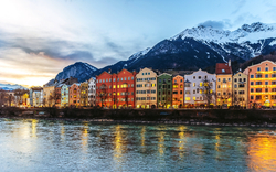 Innsbruck im Winter, bunte Häuser am Flussufer vor schneebedeckten Alpen.