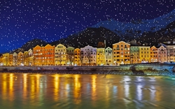 Bunte Häuserreihe in Innsbruck, reflektiert im Fluss bei Nacht, Schneefall in den Alpen.