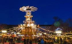Weihnachtsmarkt am Abend mit leuchtender Pyramide, festlichen Lichtern und vielen Besuchern.