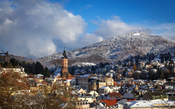 Verschneite Stadtansicht mit einer Kirche und Hügeln im Hintergrund.