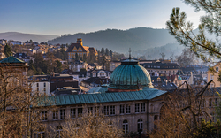 Stadtansicht mit historischen Gebäuden und Hügeln im Hintergrund bei Sonnenuntergang.