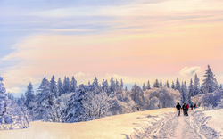 Verschneite Winterlandschaft mit Spaziergängern unter farbigem Himmel