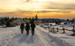 Drei Personen spazieren im Schnee bei Sonnenuntergang.