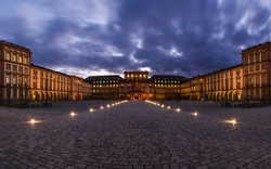 Panorama des Barockschlosses bei Dämmerung mit beleuchtetem Innenhof.