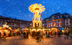 Weihnachtsmarkt mit beleuchteter Pyramide und schneebedeckten Ständen bei Abenddämmerung.