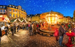 Weihnachtsmarkt bei Nacht mit Menschen und beleuchtetem Karussell im Schnee.